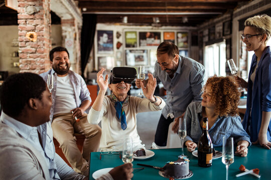 Diverse group of people laughing with senior woman using VR headset at office party - Powered by Adobe