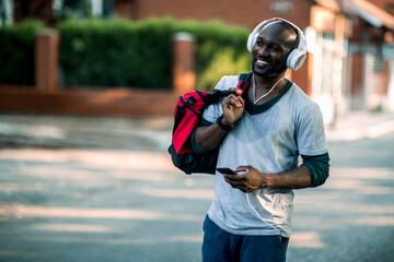 Happy man with gym bag and headphones using smartphone