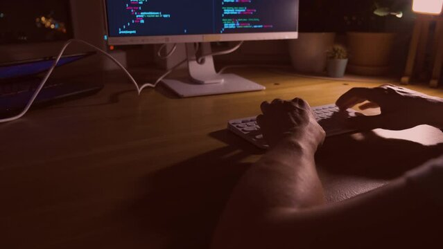 A young man programmer coding on a laptop in the dark with a view of the lights of the night city, color lighting in the room. Coding and hacking concept. Saint Petersburg, Russia - 20 April 2024