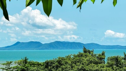 Beautiful seascape with Lush green foliage frames a vibrant blue sea with distant mountains on the horizon, ideal for travel and summer vacation themes, inspiring exploration and relaxation
