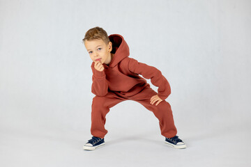 Little boy in hip hop dance position.Little boy model. Little boy in brown tracksuit on white background.