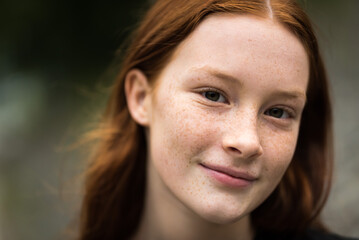Red haired twelve year old girl with freckles posing with a city bokeh background