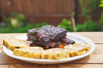 Traditional and delicious dish from cuisine of Czech Republic. Slowly roastad tender beef ribs served with carlsbader bread dumplings as a side dish on the white porcelain plate outside in the garden.