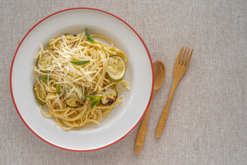 Spaghetti with grilled zucchini, parmesan cheese, spices on ceramic plate over cotton fabric background.