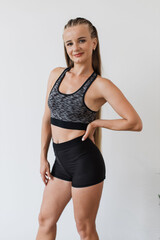 Obraz premium Young female athlete stands confidently in studio, showcasing her fitness attire. Confident female serene expression and detailed sporty hairstyle, which complements her toned physique.