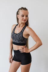 Young female athlete stands confidently in studio, showcasing her fitness attire. Confident female serene expression and detailed sporty hairstyle, which complements her toned physique.