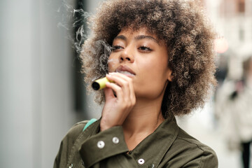 Relaxed curly woman holding an e-cigarette outdoors.
