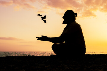 A man is sitting on the beach and playing stones