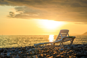 A white beach chair is sitting on a rocky beach near the ocean