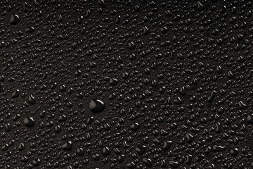 a large drop of water around which small drops on a black plastic surface