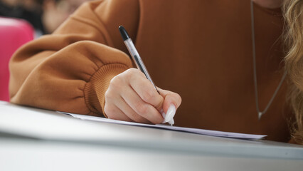 A girl is writing a dictation, preparing an answer in an exam, or filling out documents in the classroom, sitting at a desk .Photo. Selective focus. Close-up