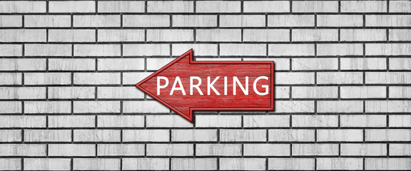 Red wooden arrow sign with the inscription PARKING hanging on a white brick wall. Left arrow pointer