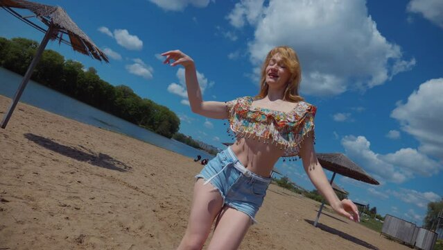 Woman dancing bachata, salsa and kizomba on the beach against the background of the blue sky. Smiling Woman barefoot poses and dances seductively on hot sand. Beach scene with girl enjoying the moment