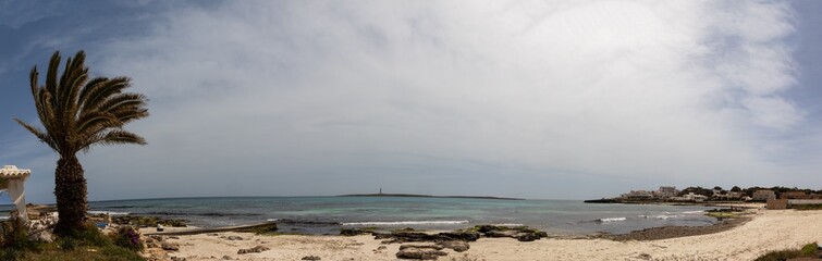 Punta Prima beach in Menorca with fine white sand and transparent waters. In the background the island of the air with its lighthouse. Spain