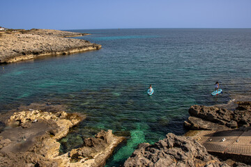 Two girls paddle surfing in the turquoise blue waters of the wonderful Cala Torret in Menorca, Spain