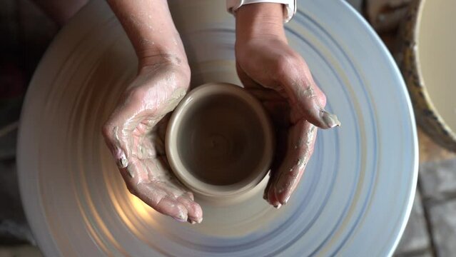 Dobele, Latvia- August 18, 2023 - Potter making ceramic pot on the twisted pottery wheel. Top view. Potter at work, close up. Handmade, craft. White clay. Slow motion