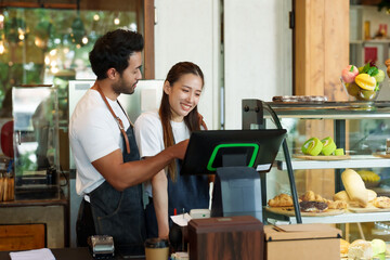 Owner of a small cafe, business couple Multiracial men beautiful Asian wives stand smile. Looking cafe's order sales summary machine behind the cash register counter. Next bread bakery cabinet.