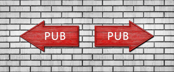 Red wooden arrow signs with the inscription PUB hang on a white brick wall. Right and left arrow...