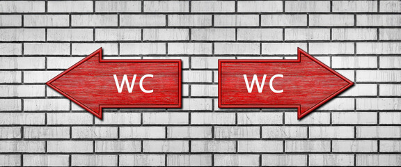 Red wooden arrow signs with the inscription WC hang on a white brick wall. Right and left arrow pointers. Set direction