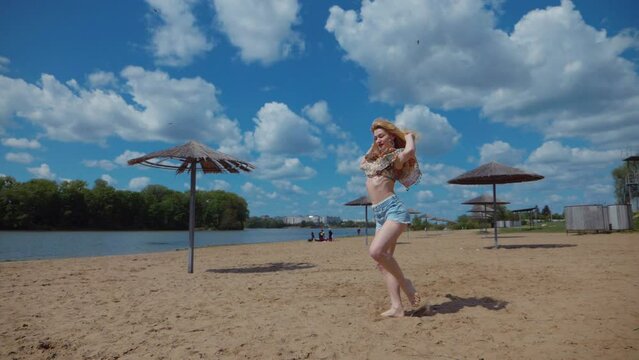 Woman dancing bachata, salsa and kizomba on the beach against the background of the blue sky. Smiling Woman barefoot poses and dances seductively on hot sand. Beach scene with girl enjoying the moment