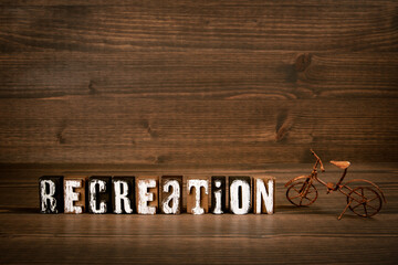 RECREATION. Text from alphabet blocks and rusty miniature bicycle on wood texture background