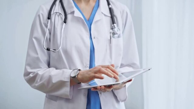 Female doctor using digital tablet in clinic. Healthcare professional with a stethoscope around her neck operating a touchscreen computer while standing on the glass background. Medicine and