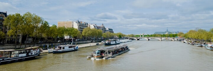 Fototapeta premium Panoramic view of the Seine River with tour boats in Paris, France, on a sunny day, ideal for travel, tourism, and European holidays concepts