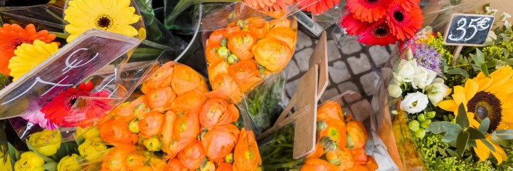 Assorted colorful fresh-cut flowers for sale at a market stall with prices displayed, ideal for...