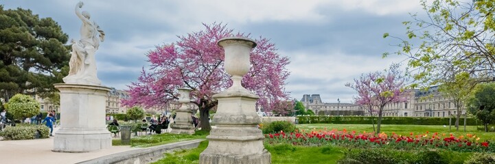 Elegant springtime scene in a European park with blooming cherry blossoms and classical sculptures,...
