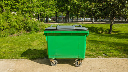 Bright green waste container in a sunlit urban park setting, symbolizing environmental conservation and cleanliness, suitable for Earth Day and public service campaigns