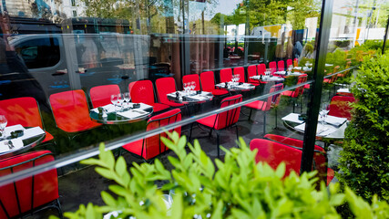 Outdoor dining setup at a modern restaurant with red chairs and tables set for service, reflecting city life and suitable for concepts related to dining out and urban lifestyle