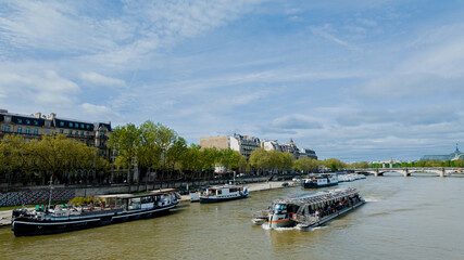 Naklejka premium Scenic view of the Seine river with tour boats and Parisian architecture, ideal for travel, tourism, and French culture themes