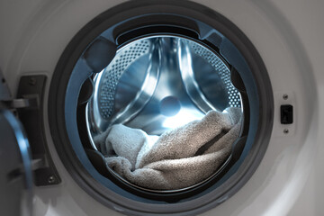 Opened washing machine drum with towel. Closeup. Front view. Washing dirty clothes in the washer.