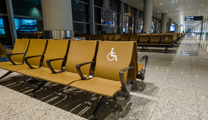 Empty airport waiting area with rows of brown seats and designated handicapped seating, indicative...