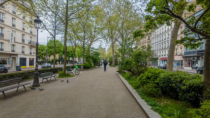 Tranquil urban park in spring with fresh greenery, walking pedestrians, and classic streetlamps,...