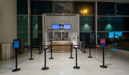 Empty airport gate with stanchion barriers at night, suggesting concepts of travel, business trips,...