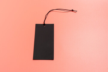 Black label with black cord with space for writing on a pink background. Black label on a pink...