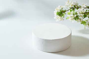 Empty round white podium for product presentation and spring flowers on a light background. Mockup...