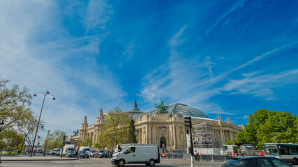 Sunny cityscape with blue sky featuring European classical architecture and busy street traffic,...
