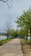 Individual jogging on a tranquil riverside path in spring, promoting fitness and Earth Day activities, amidst budding trees and clear skies