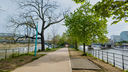Tranquil riverside walkway with budding trees in early spring, ideal for urban tranquility themes and outdoor exercise in city settings