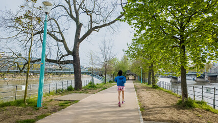 Active woman jogging along a scenic river pathway in spring, promoting health and fitness, suitable for International Women's Day and National Running Day themes