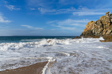 Le sable de la plage recouvert d'écume blanche, avec une falaise en bout de plage, une scène...