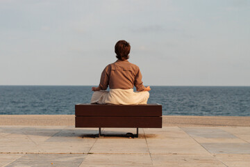 a young girl sits with her back alone on the beach in the lotus position