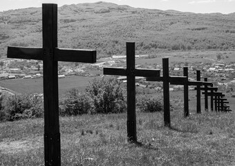 A row of crosses on a hill and in the background the houses of a village, in black and white