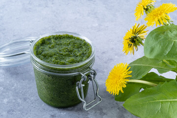 Dandelion greens pesto in jar on a gray background, side view. Appetizer, condiment or topping....