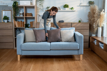 Fototapeta premium A person arranges pillows on a comfortable sofa, creating an inviting atmosphere while maintaining an organized, cozy home environment.