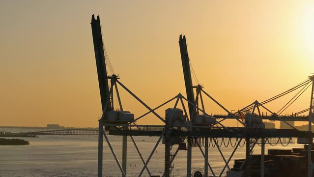 Drone shot of huge silhouette cranes by sea against clear orange sky at Miami port during sunset