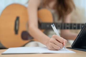 A woman sitting on a couch, strumming a guitar, and writing music notes in a notebook, creating...