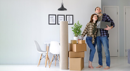 Happy young married couple are moving to new apartment, man and woman standing in a new house,...